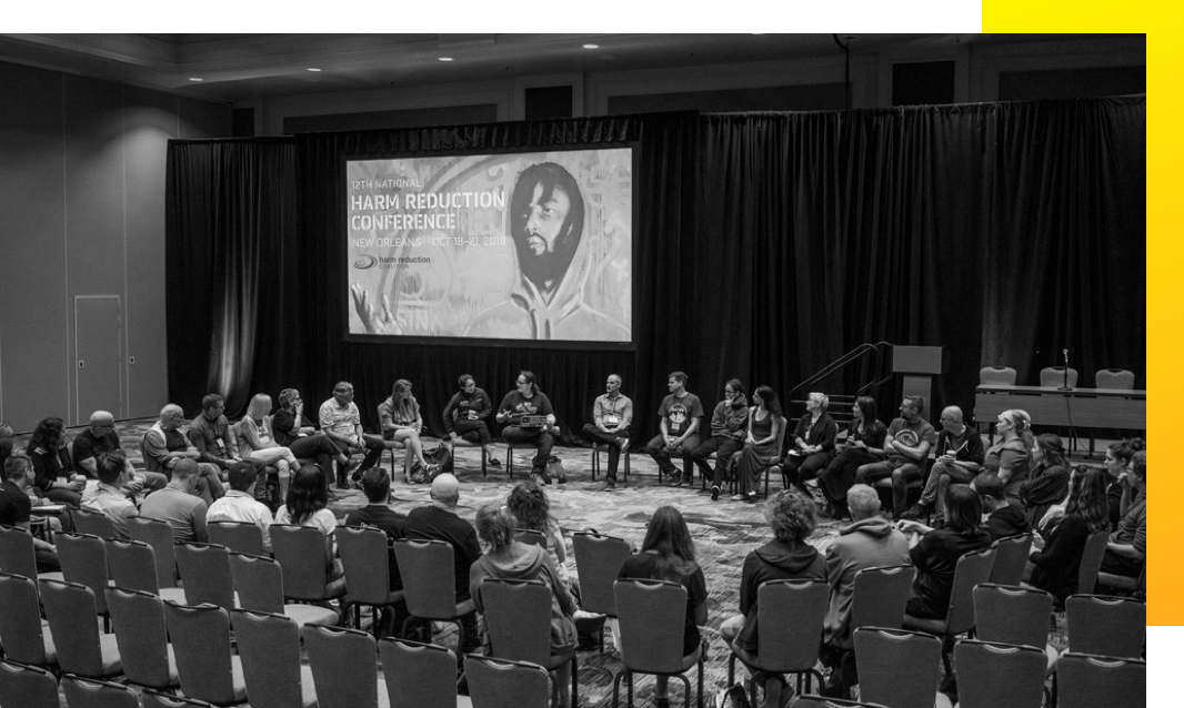 Group of about 40 people sitting in chairs gathered in a circle, engaged in a discussion at the 12th National Harm Reduction Conference in New Orleans