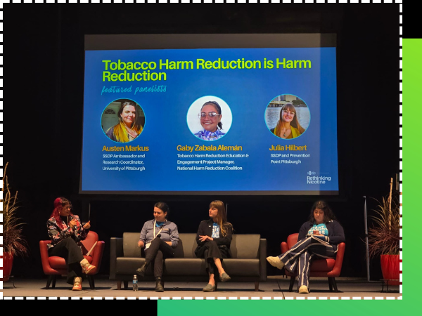 Panel of four speakers sit on stage under a projector screen with the introductory slide reading "Tobacco Harm Reduction is Harm Reduction"